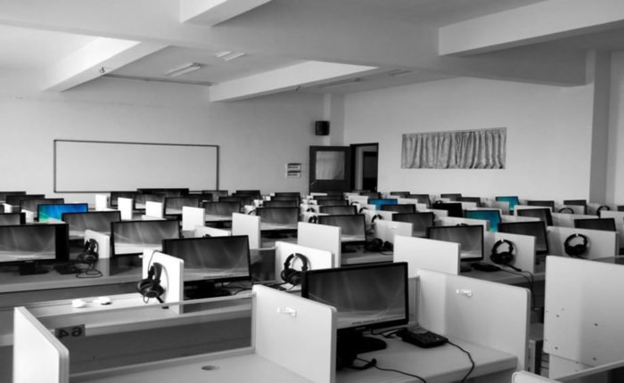 Empty office of cubicles that each have a desktop computer and headset.