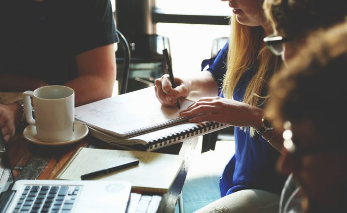 Group of people meet and take notes in a notepad over coffee.