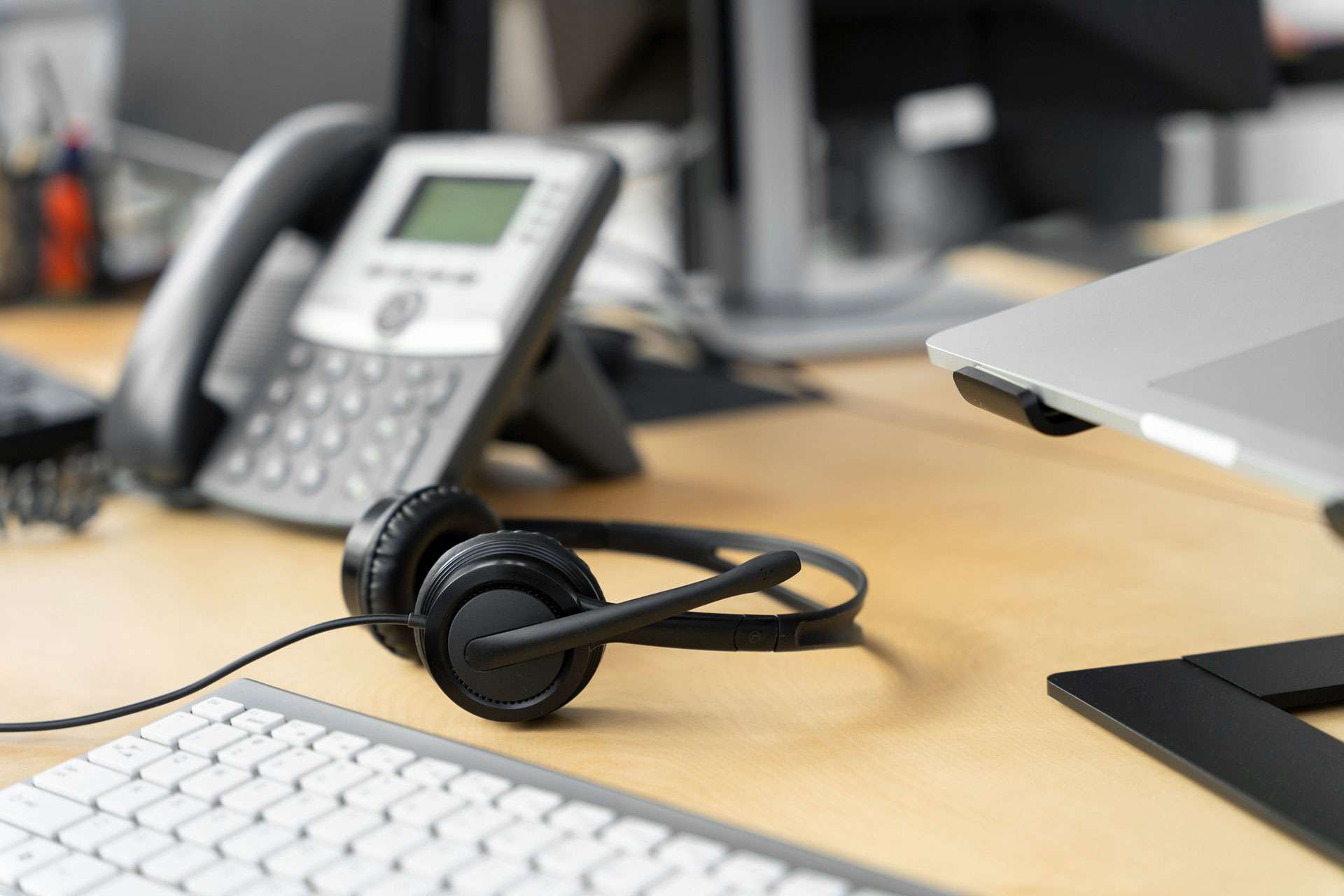 A headset site on a table in focus with a blurred background of a telephone.