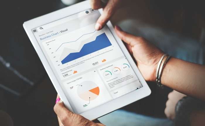 Two people view a tablet that contains graphs of business charts.