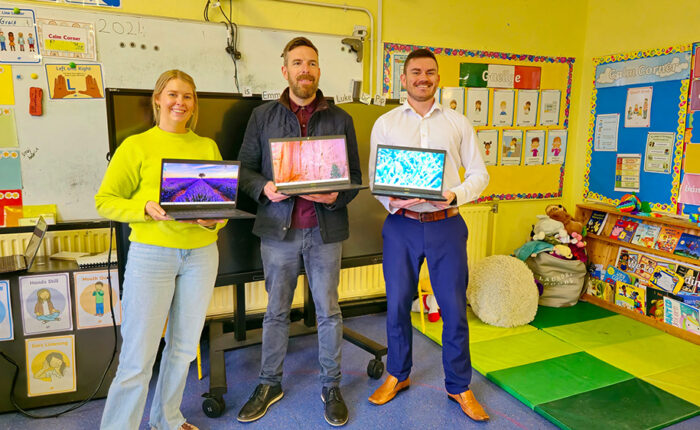 Three people posing with three open laptops.