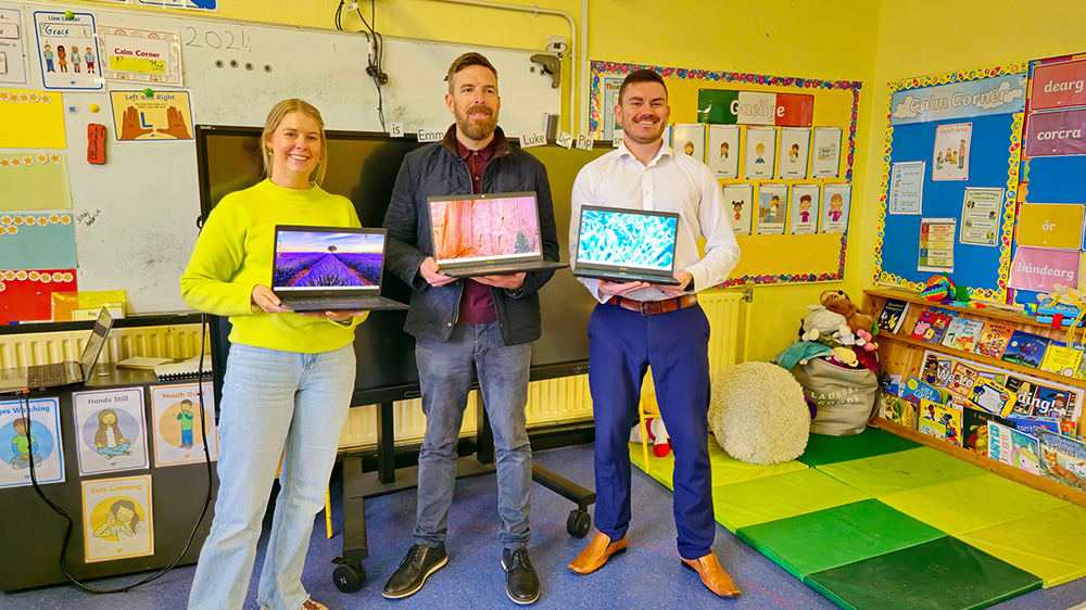 Three people posing with three open laptops.