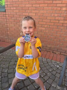 Young girl showcases her medal while wearing a yellow t-short with Bluescope logo.