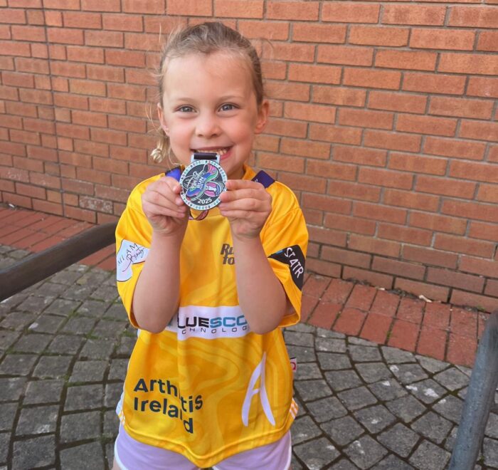 Young girl showcases her medal while wearing a yellow t-short with Bluescope logo.