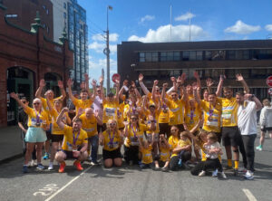 Group of people wearing yellow t-shirts for Arthritis Ireland with Bluescope logo on front raise hands in the air.