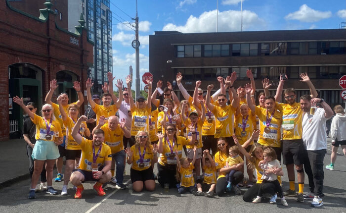 Group of people wearing yellow t-shirts for Arthritis Ireland with Bluescope logo on front raise hands in the air.