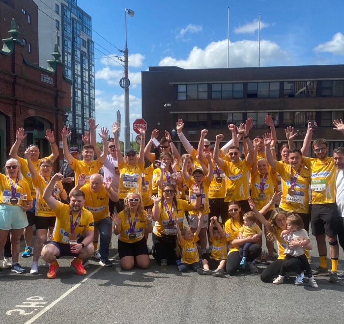 Group of people wearing yellow t-shirts for Arthritis Ireland with Bluescope logo on front raise hands in the air.