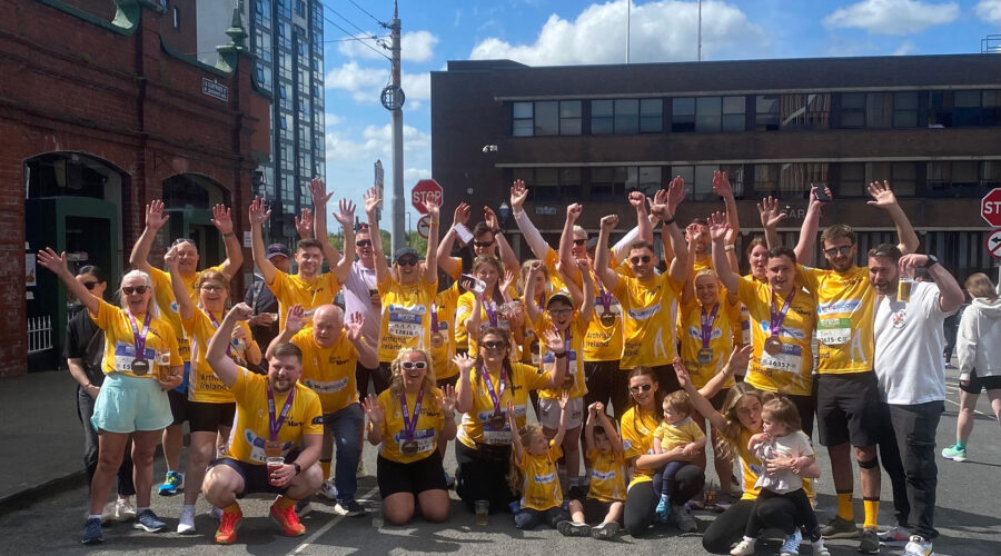 Group of people wearing yellow t-shirts for Arthritis Ireland with Bluescope logo on front raise hands in the air.